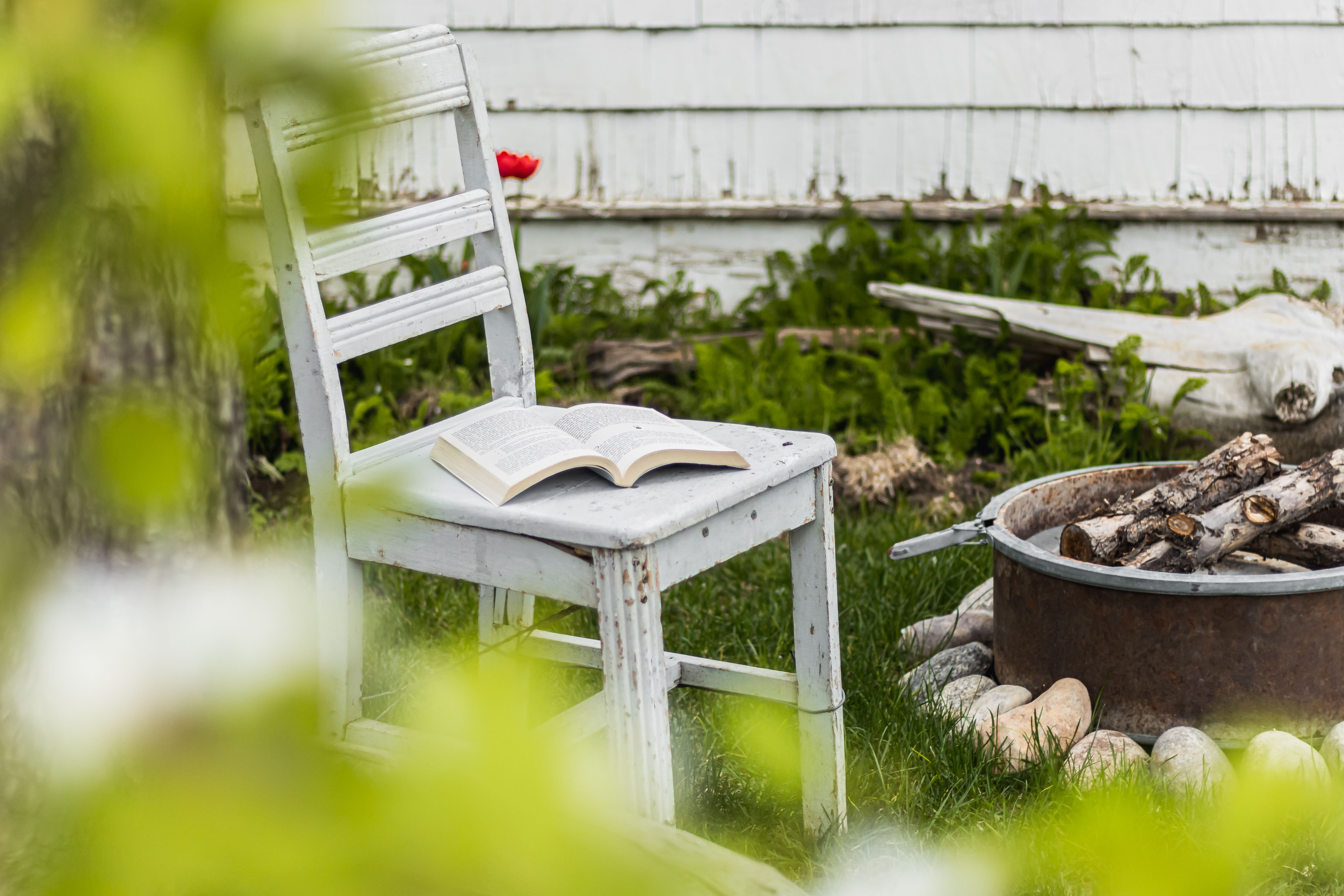 Book on a chair beside a backyard fire pit surrounded by nature