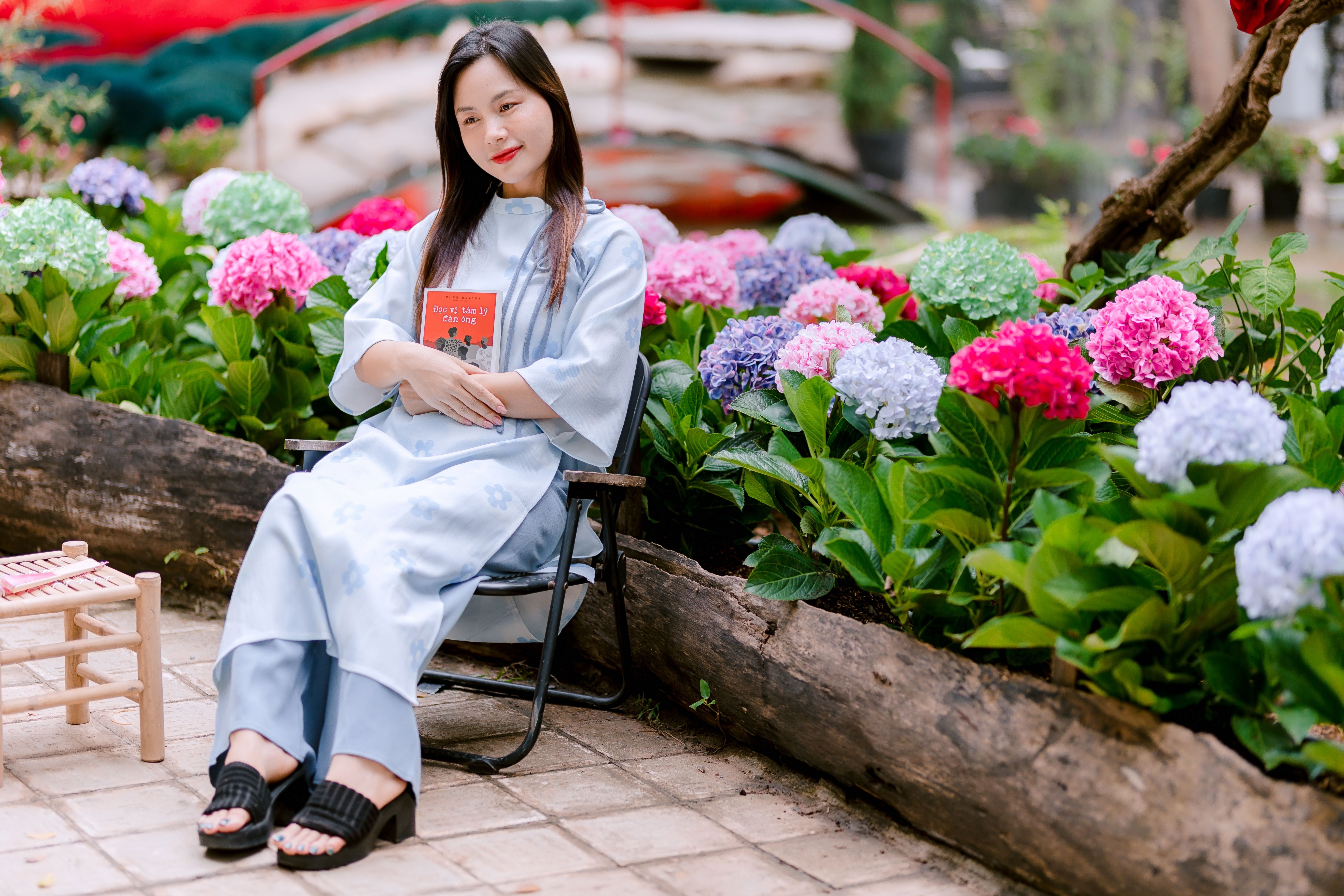 Woman sitting in a garden surrounded by colorful hydrangeas holding a book