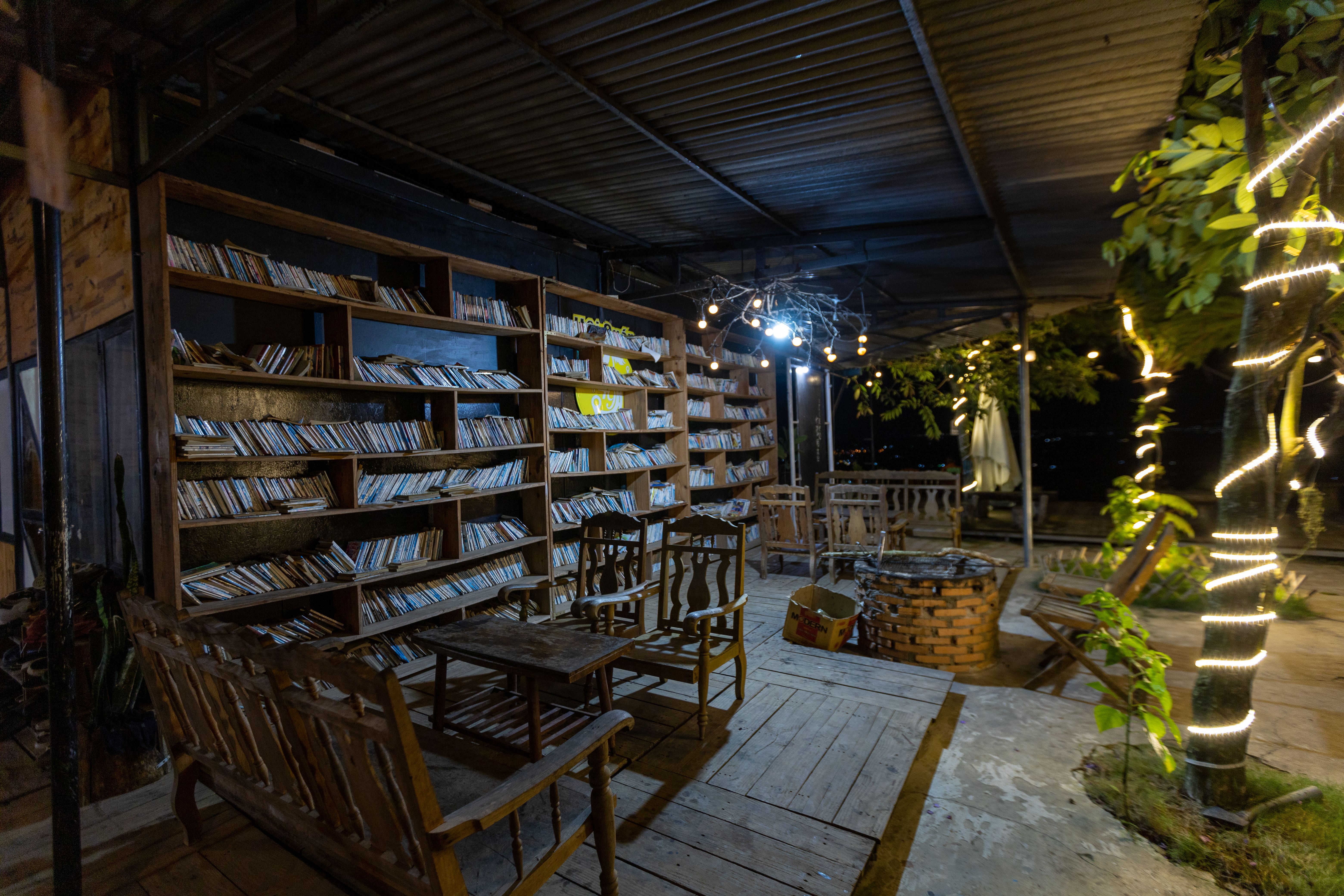 Tranquil outdoor reading area with wooden chairs and bookshelves under string lights